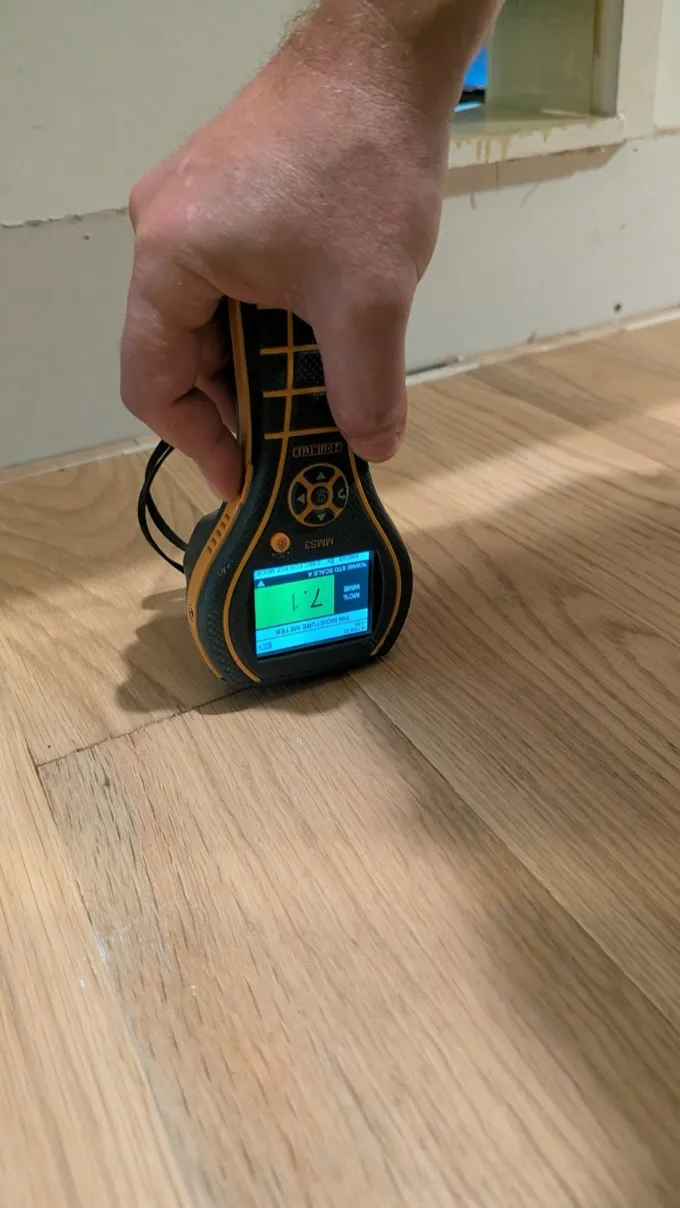 Technician checking a hardwood floor with a moisture meter during a water damage inspection